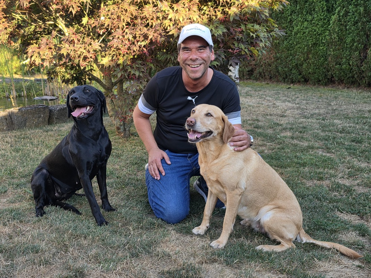 Oliver, Mitarbeiter bei Pudelwohl365, mit seinen Labradorhündinnen Kim und Raven im Garten